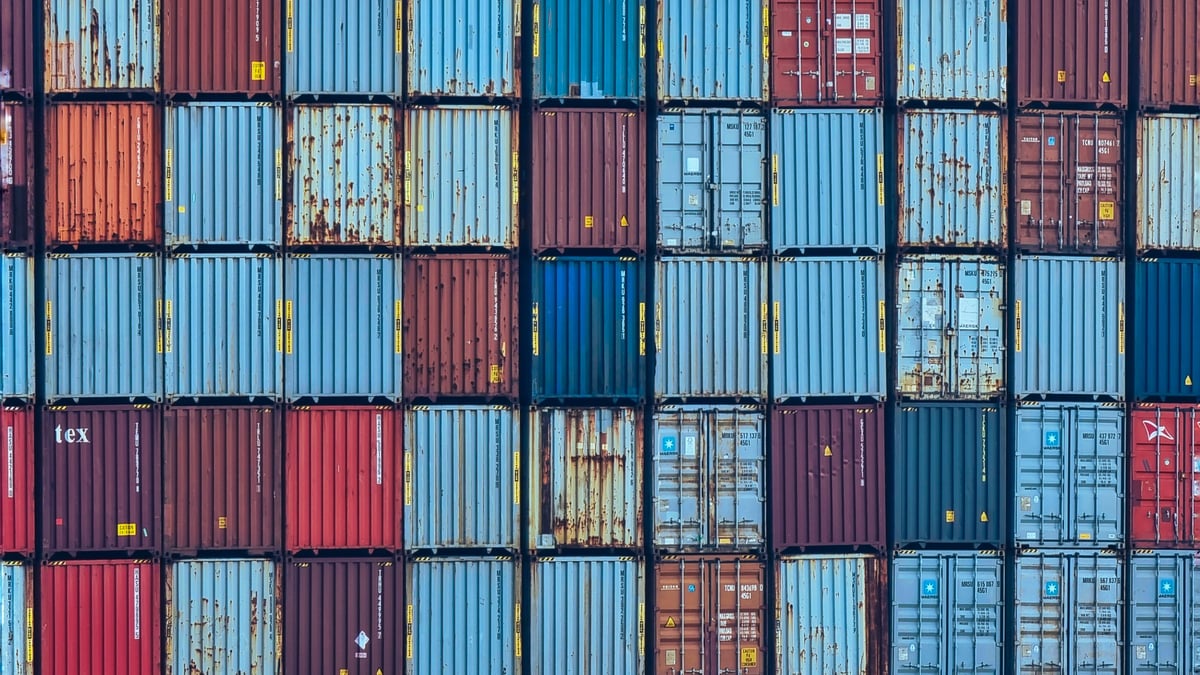 A high-resolution image showcasing a seamless pattern of stacked cargo containers. The arrangement forms a grid of square and rectangular shapes, creating a visually striking geometric composition. Ideal for use in industrial, logistics, or global trade themes, this image highlights symmetry, structure, and the organized chaos of shipping yards. The bold colors and repetitive design make it perfect for backgrounds, presentations, or editorial content focused on commerce, transportation, or infrastructure.